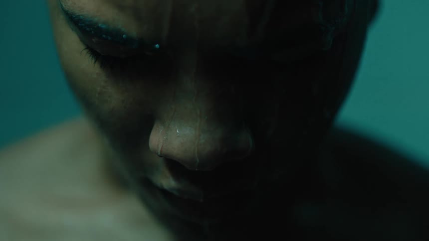Close up of a mans face with water running down it as he looks downward