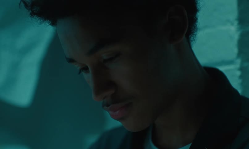 A close up of a young males face as he looks down blinking before looking up and speaking to someone in front of him