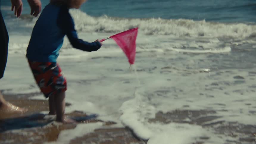 Blonde boy with his mom at the beach playing with a pink fishing net on the water