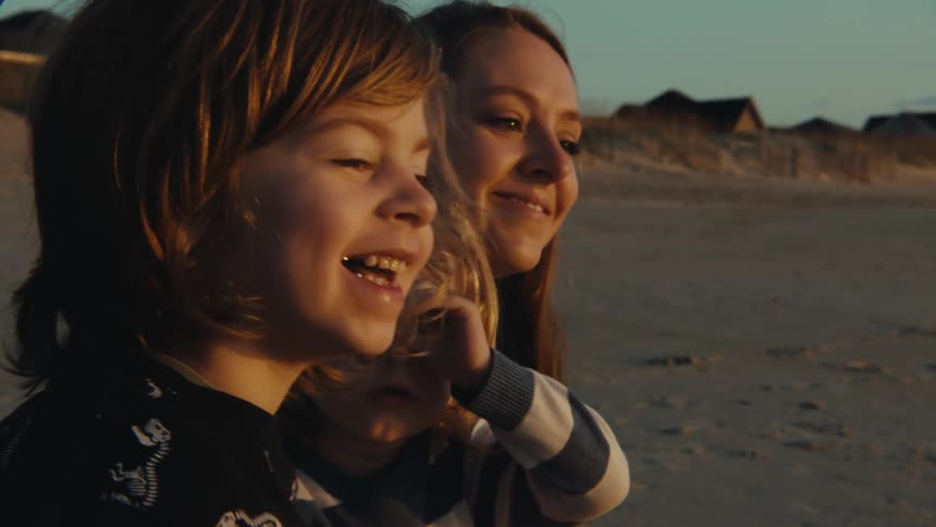 Family of a mother with two children sitting at the beach and smiling during dusk or dawn