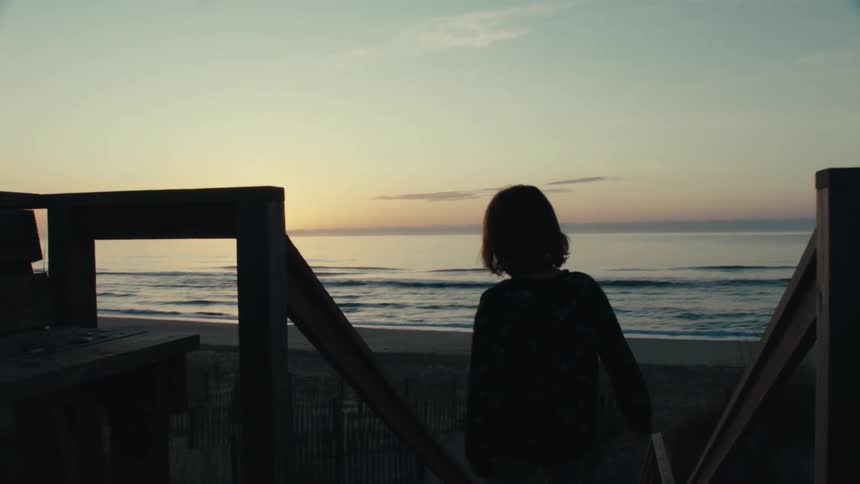 Silhouette of a young child walking down outdoor steps toward the beach as the sun sets