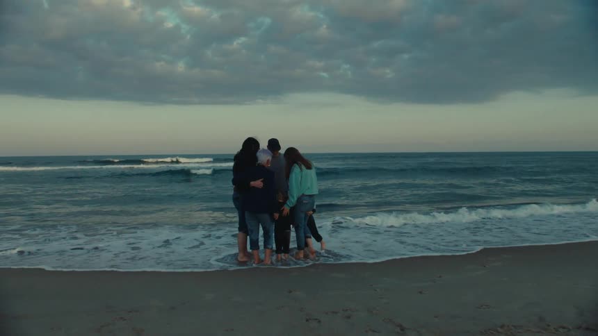 A family group hug near the ocean at the beach