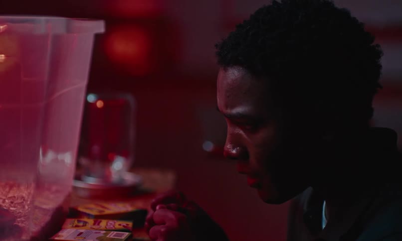 Nervous black man or teenager kneels down and then stands up in front of a table with objects on it