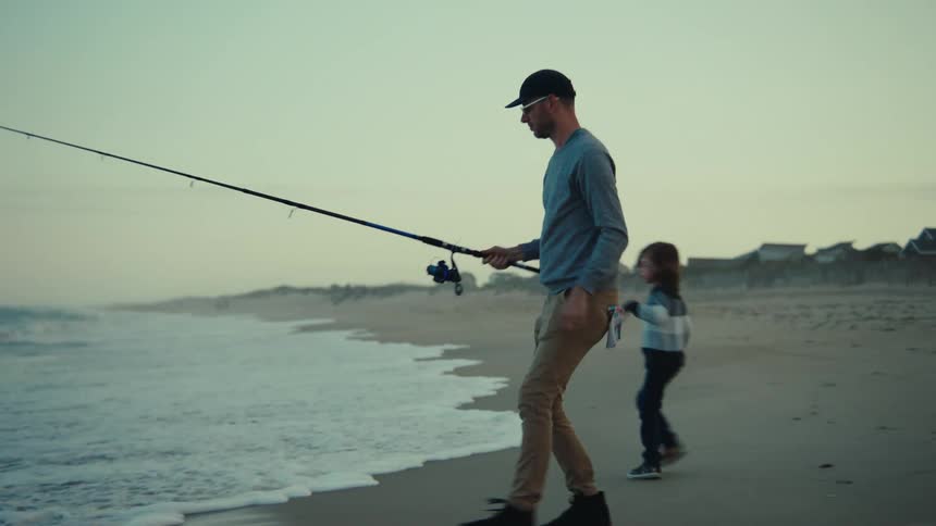 A man casts his fishing rod in to the water as his children play on the beach with their mother