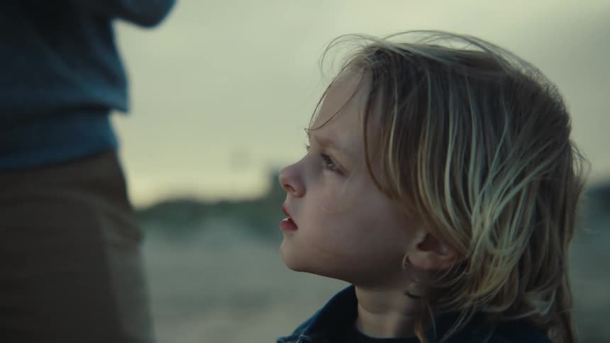 A father and son are fishing on a beach while the son offers a shrimp