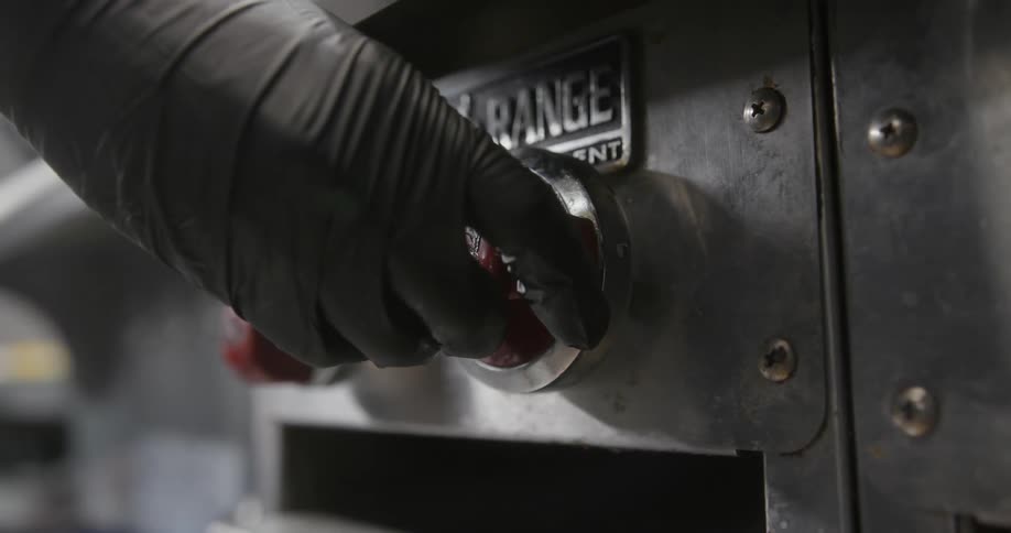 Cook wearing gloves adjust knob on kitchen range