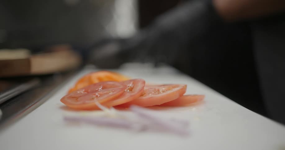 Person wearing gloves chopping tomatoes and vegetables on a kitchen counter