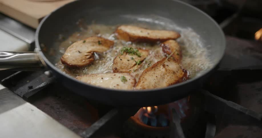 Chicken breasts being cooked in a frying pan with parsley sprinkled over them
