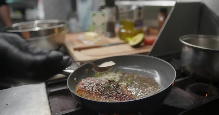 Person wearing gloves cooking meat in a frying pan