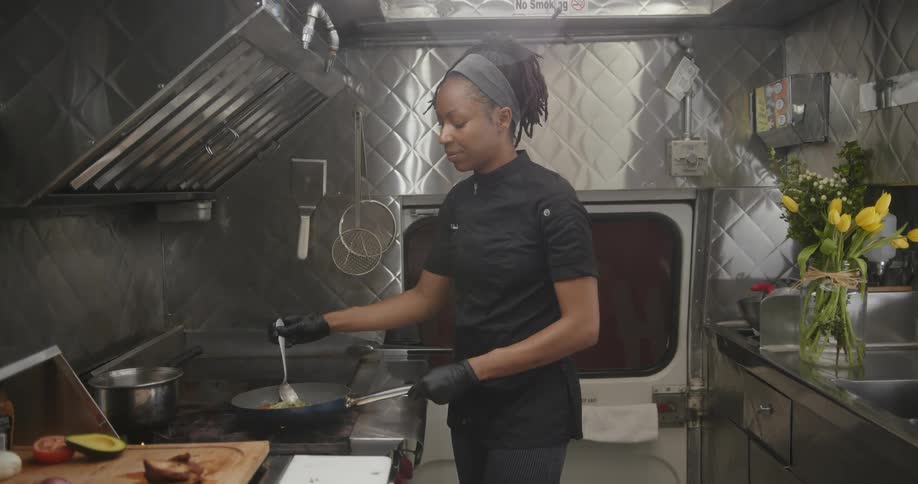 Woman stands at stove in galley kitchen stirring skillet