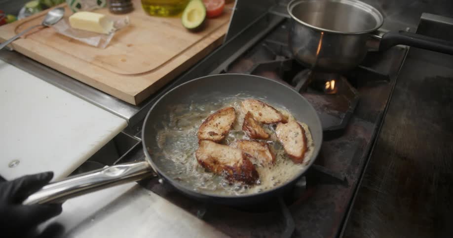 Person wearing gloves cooking meat in a frying pan on the stove