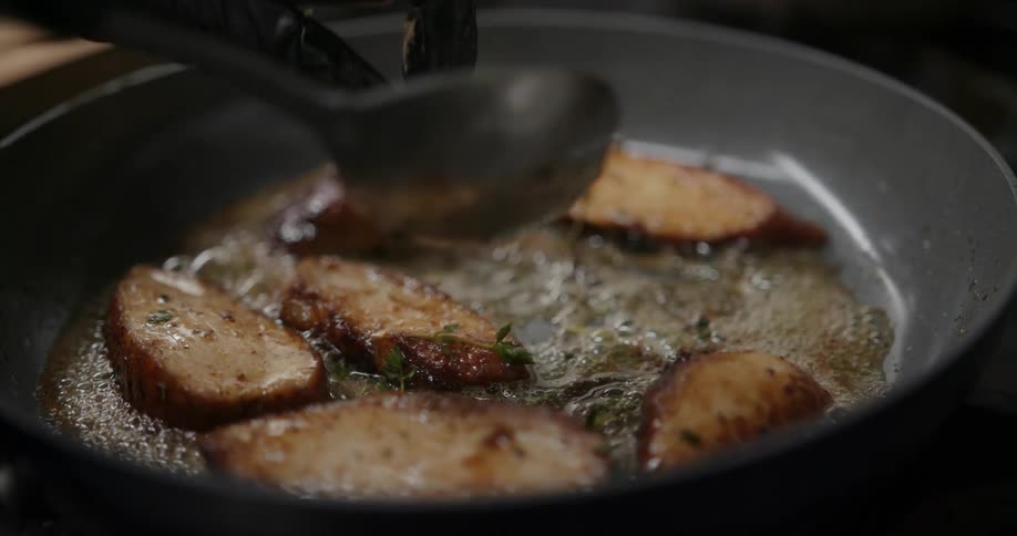 Close up of a persons hands using a spooin to turn over food cooking on a hot pan