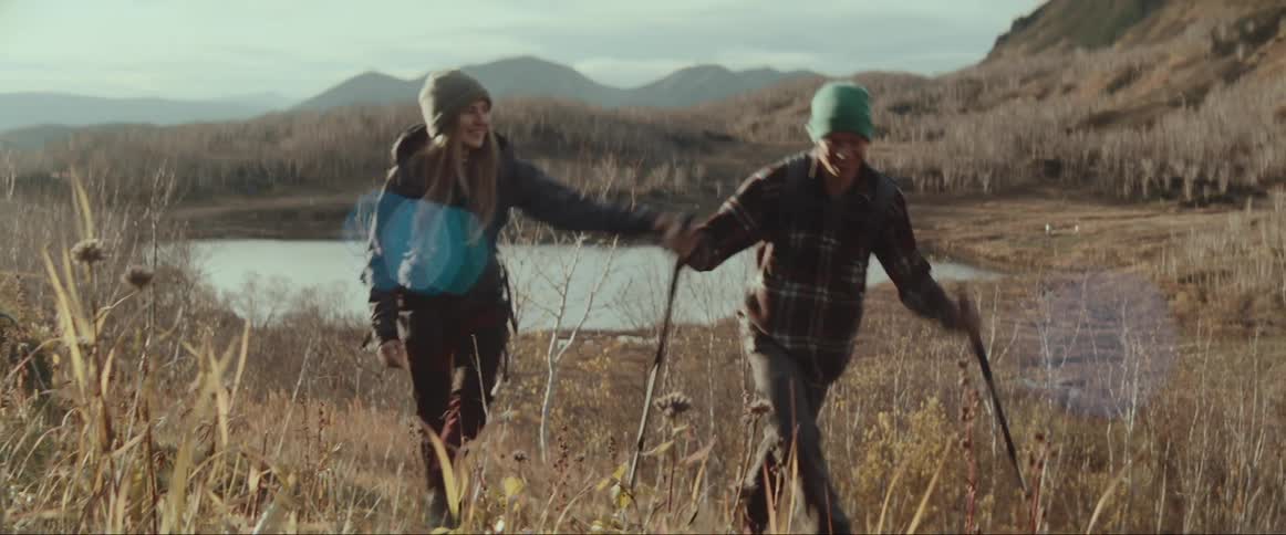 A woman playfully shoves a man as they hike together up a hill in the wilderness during the day