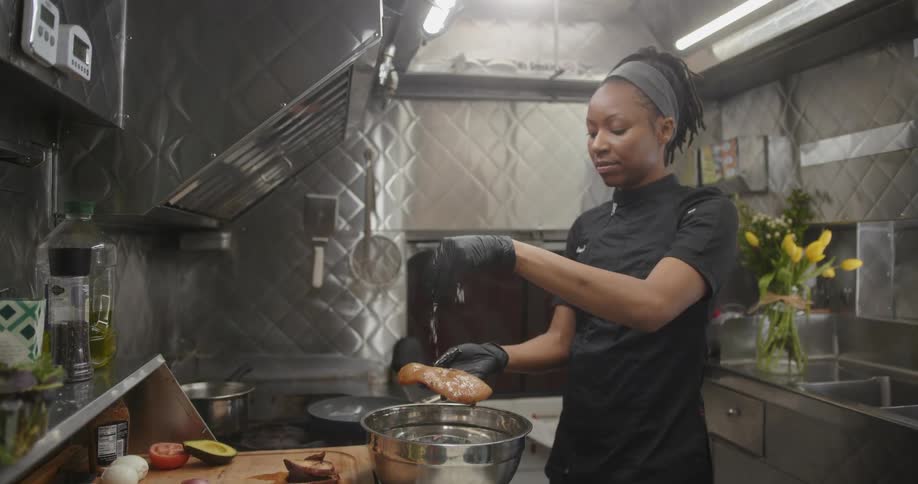 A woman chef wearing gloves seasoning meat in the kitchen