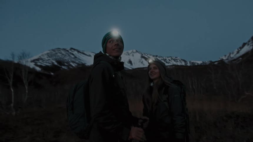 A man and woman stop while climbing a snowy mountain to look around and take in the scenery