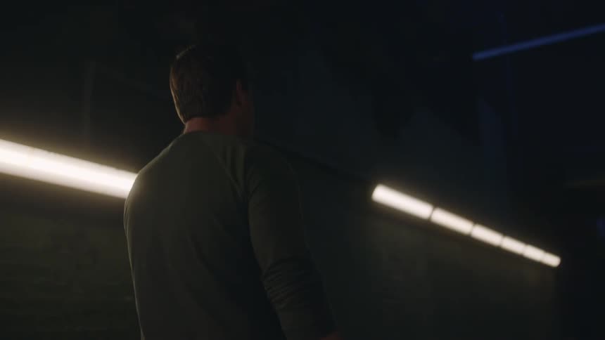 Man walks from brightly lit to dimly lit portion of hallway then stops to make a phone call