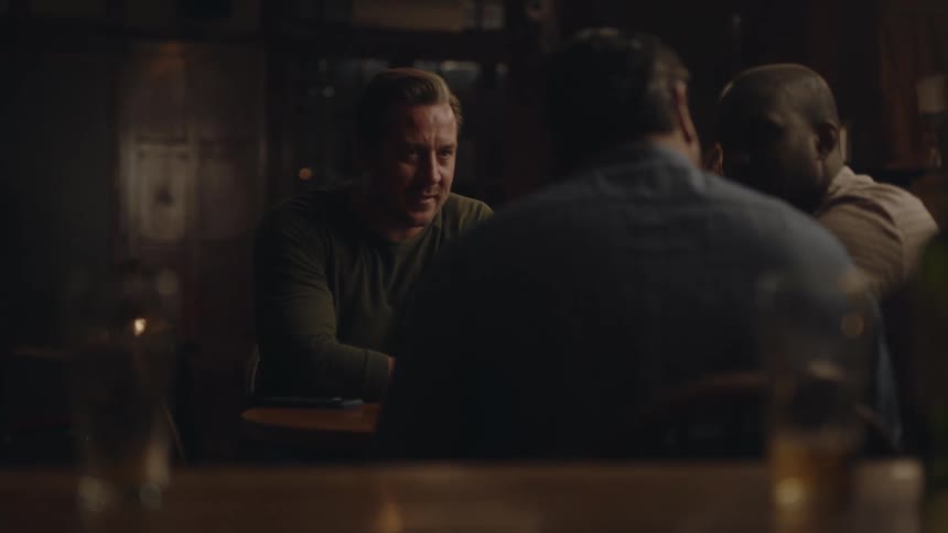 Three men sit down in a bar for drinks while one of them looks at his phone