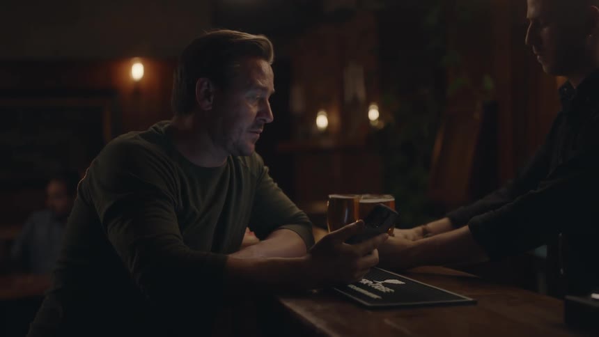 A man looks at his phone while waiting at the bar for drinks