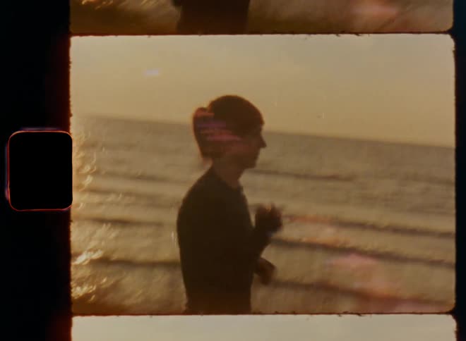 Shaky Super 8 mm film footage of an independent brunette woman with ponytail and red headband wearing workout clothes while jogging alone at the coast as healthy morning routine to lose weight and get back into shape