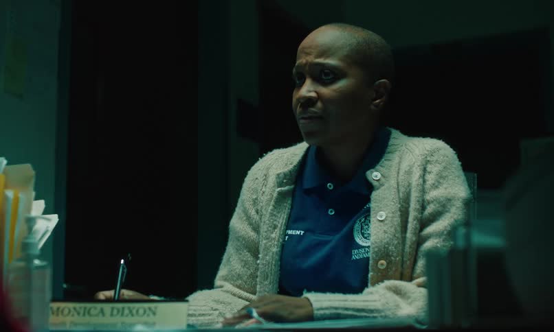 A woman sitting at a desk looks sad as she uses a pen to write something and speaks to someone