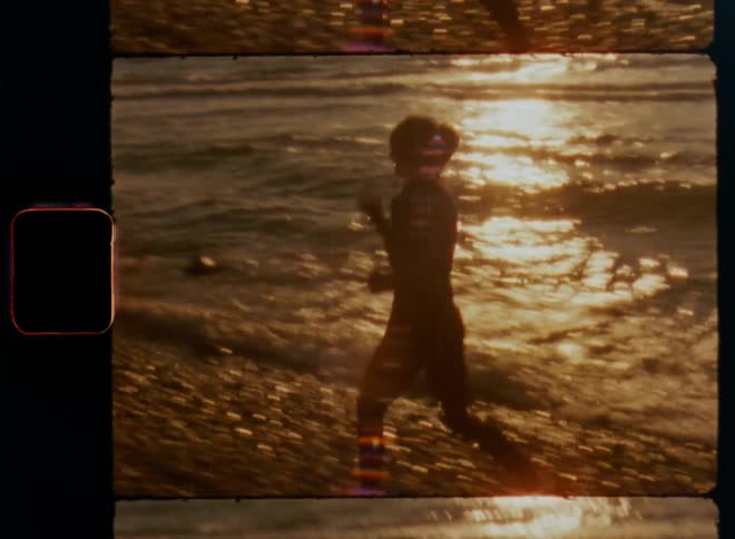 Brown-haired woman runs or jogs across gravel beach during the day enjoying sunshine and fresh coastal breeze as waves wash into the shore and water and wet stones reflect bright light of the sun on warm springtime day on vintage Super-8 mm film