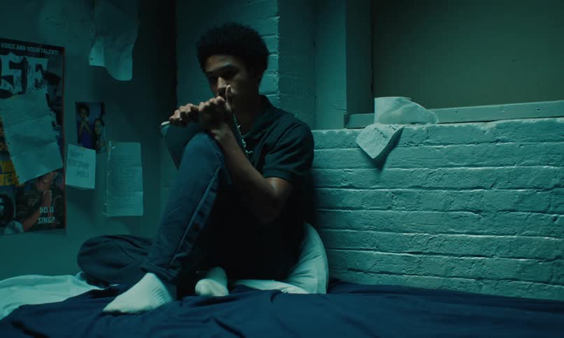 Teenage boy sitting on a bed against a white brick wall with paper tacked to the wall next to him