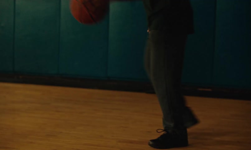 A teen boy dribbles a basketball in a school gym as another tries to block