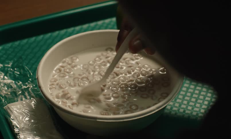 A close up of a person stirring cereal around in a bowl with a spoon on a green tray