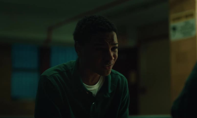 Sad and nervous young inmate dressed in a prison uniform talking to someone
