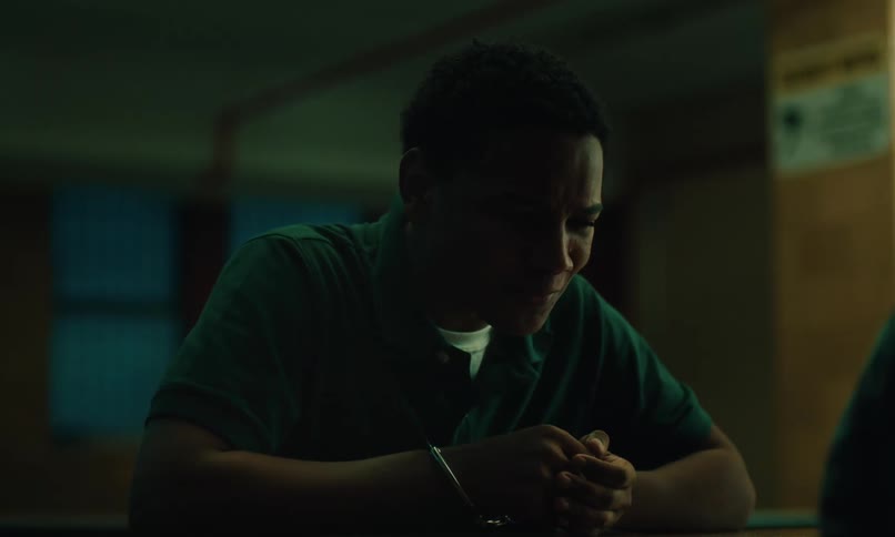 A boy in handcuffs frowns as he talks to someone