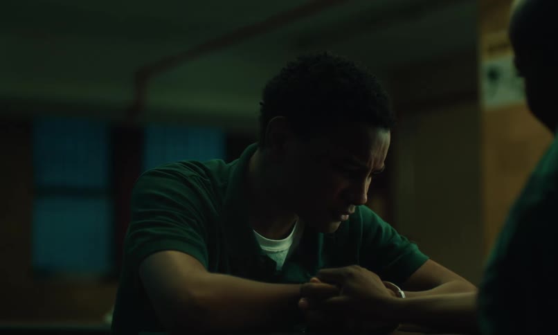 Teenage boy sitting with his arms on a table and crying as the woman in front of him puts her hand on his forearm
