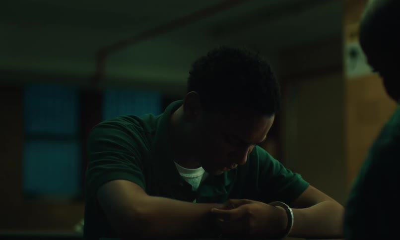 Teenage boy sitting with his arms cuffed and head down in front of a woman sitting across from himm