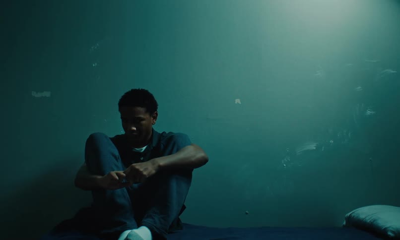A sad young inmate sitting on the bed in the cell alone