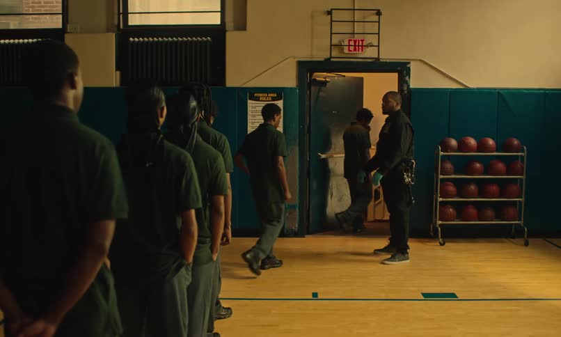 A group of teenage boys in a gymnasium lined up to get searched before walking through a doorway