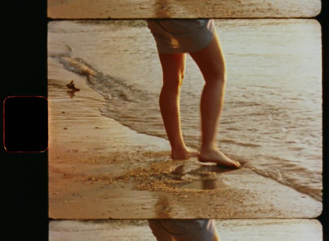 A womans legs and feet as she walks through the water on the beach and in the sand