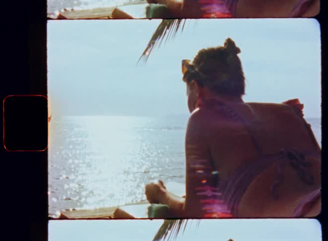 A woman in a bikini is laying on a lounger on the beach reading a book