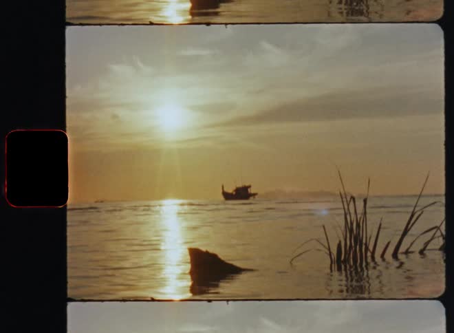 Sun shines from red sky reflecting from water near shallows and silhouetted boat