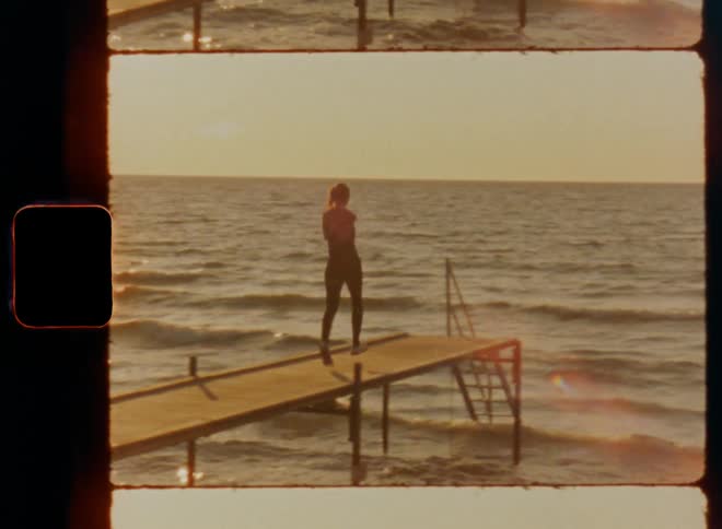 Dynamic handheld 8mm footage of female sportsman enjoying Crossfit outdoor sport workout running onto wooden deck in harbour and stopping at edge staircase as sun rises over lake or ocean with sunlight reflection and wavy water surface on windy spring day