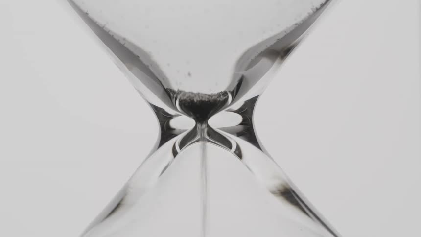 Black sand moving slowly in an hourglass to the bottom