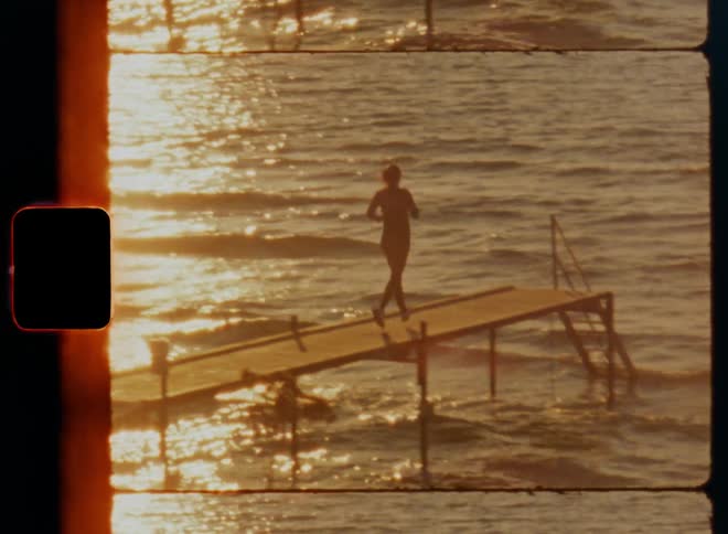 Sporty young woman jogging on landing deck in port and stopping at end in front of stairs with hand railing to enjoy view of the setting sun and fresh sea breeze that causes ripples and waves on the water surface which reflect warm sunshine light