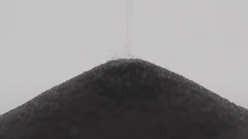 An extreme close up of black sand falling through an hourglass
