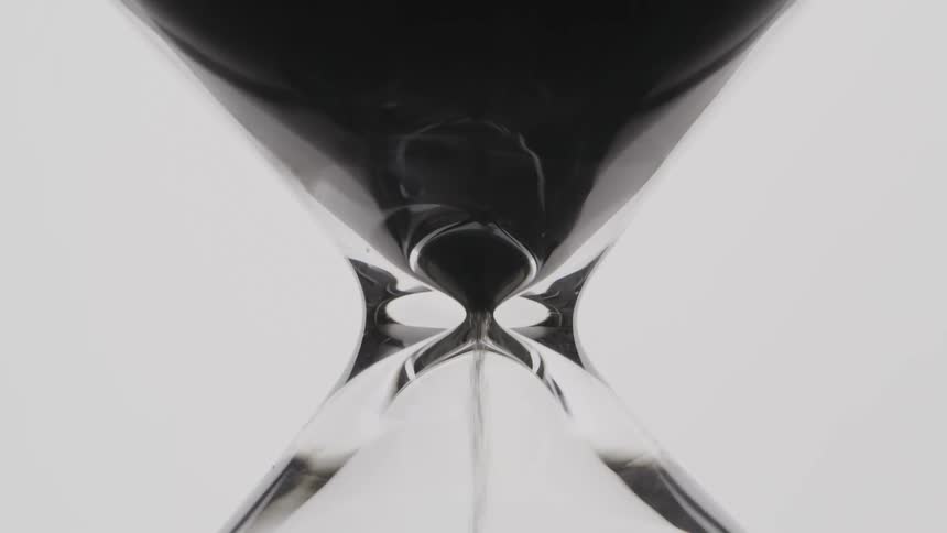 Close up of a glass timer with black sand trickling down into the bottom half