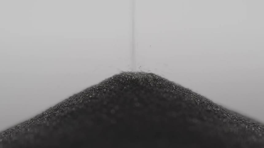 Small gray granules flow downward to form mound against a gray background