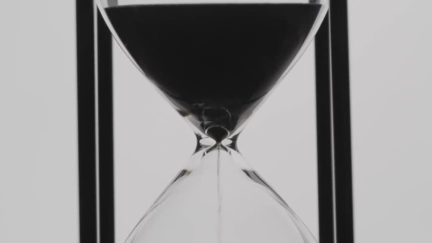 A close up of an hourglass pouring black sand into the bottom half