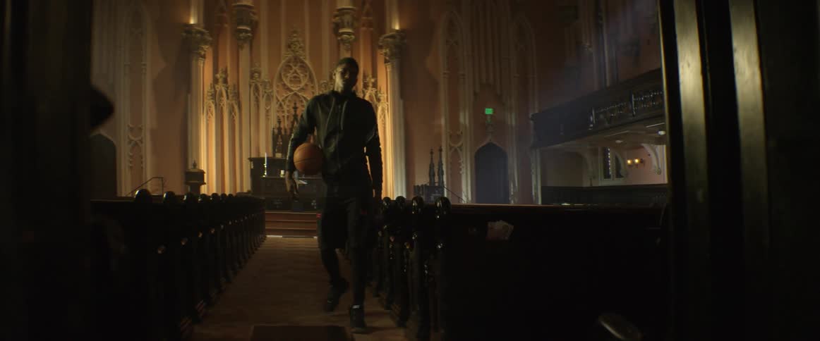 A basketball player gets up from a church pew and walks up the aisle