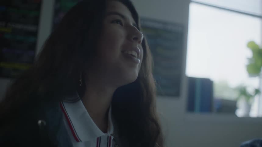 A smiling teenage girl reading a book at a round table in her classroom