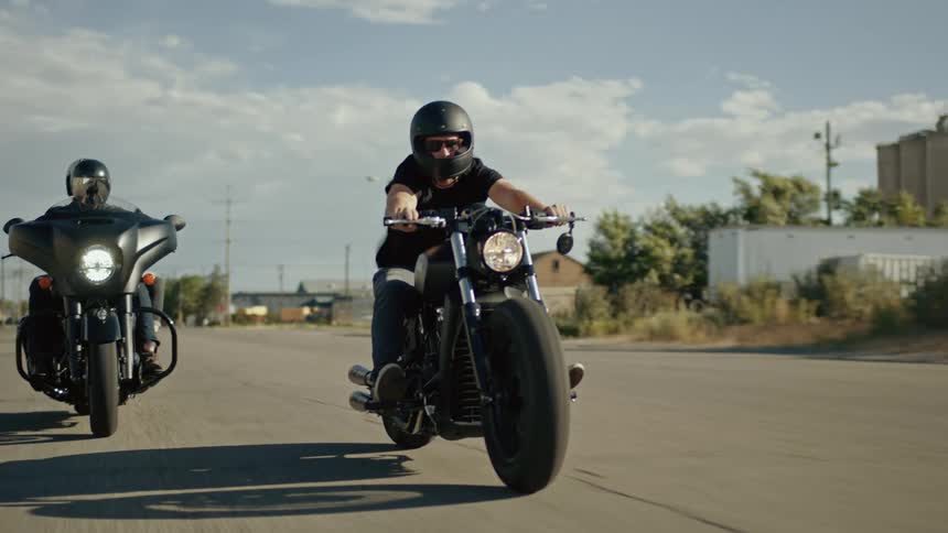 Two men driving motorcycles down the road on a bright sunny day