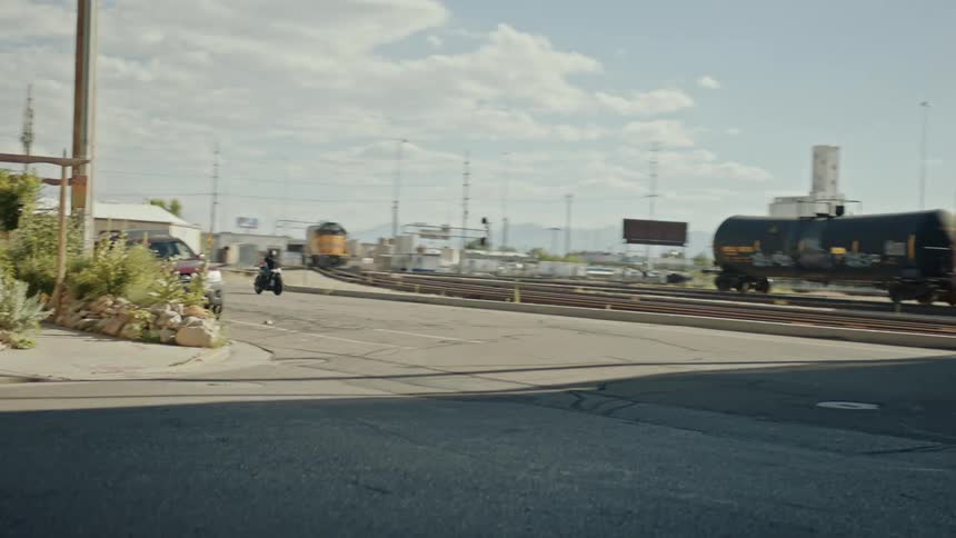 Motorcyclists pass under overpass on road paralleling train tracks