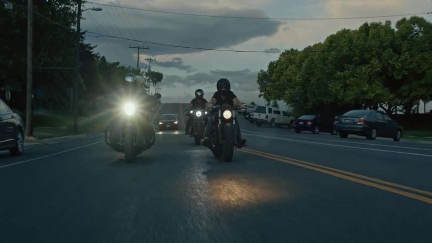 A group of motorcyclists ride together down a road in the evening
