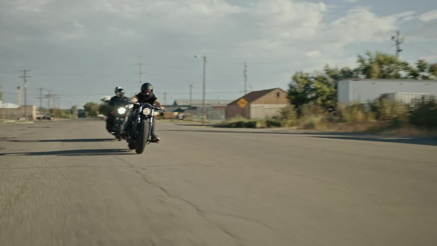 Two people speeding on their motorcycles in a sunny urban area